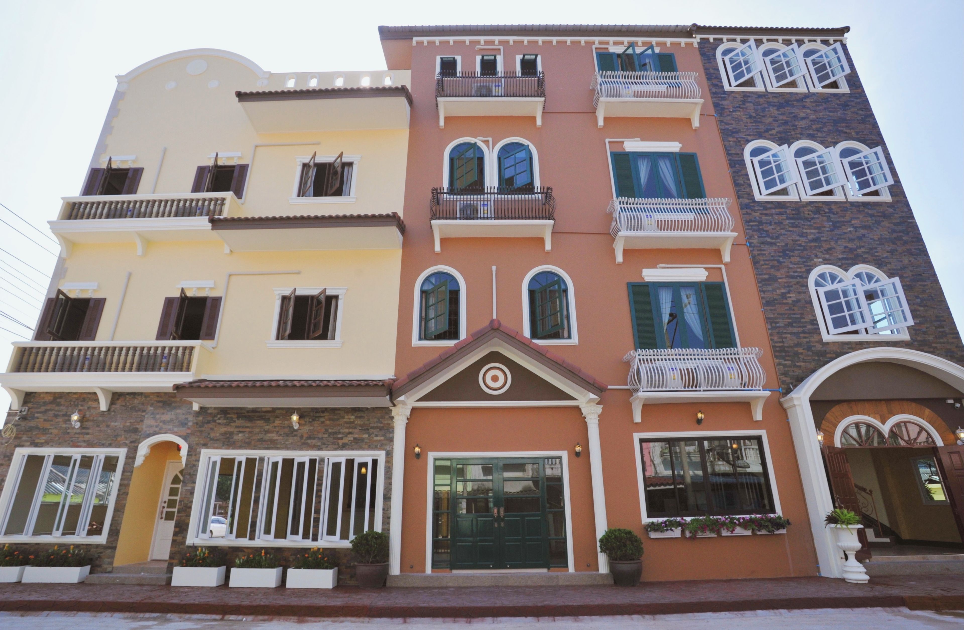 A multi-story building with balconies, a central entrance with a door, and windows with shutters.