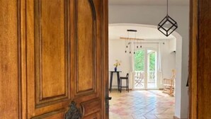 A wooden door with a brass handle, leading to a room with a tiled floor and a view of an outdoor area with a table and chairs. - Maison avec piscine 1 (Marseille)