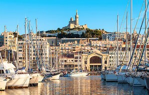 Ein Yachthafen mit mehreren vertäuten Booten, ein markantes Gebäude mit Kuppel und Turm im Hintergrund und eine dicht bebautes Stadtgebiet rund um das Wasser.