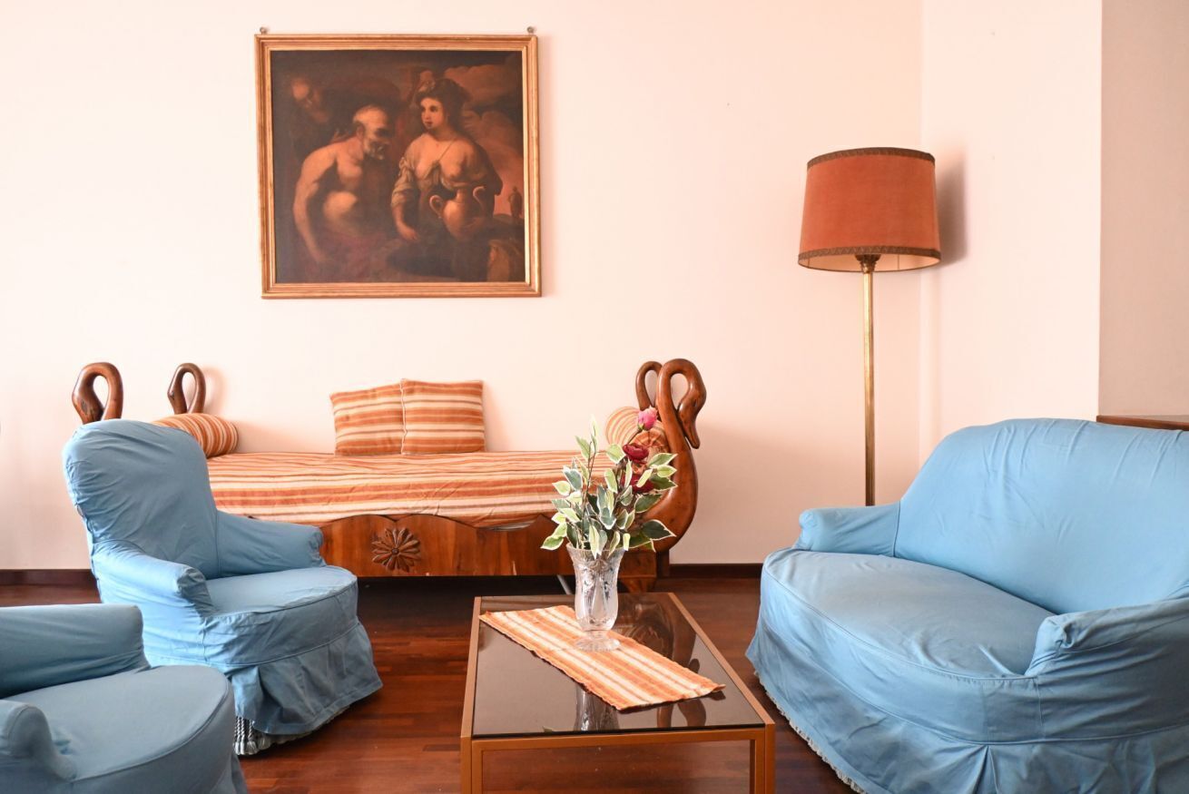 A room with a sofa, two armchairs, a coffee table, a lamp, and a painting on the wall.