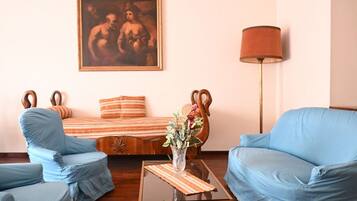 A room with a sofa, two armchairs, a coffee table, a lamp, and a painting on the wall.