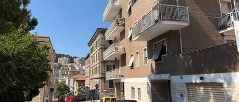 A residential street with multi-story buildings, parked cars, and a clear sky.
