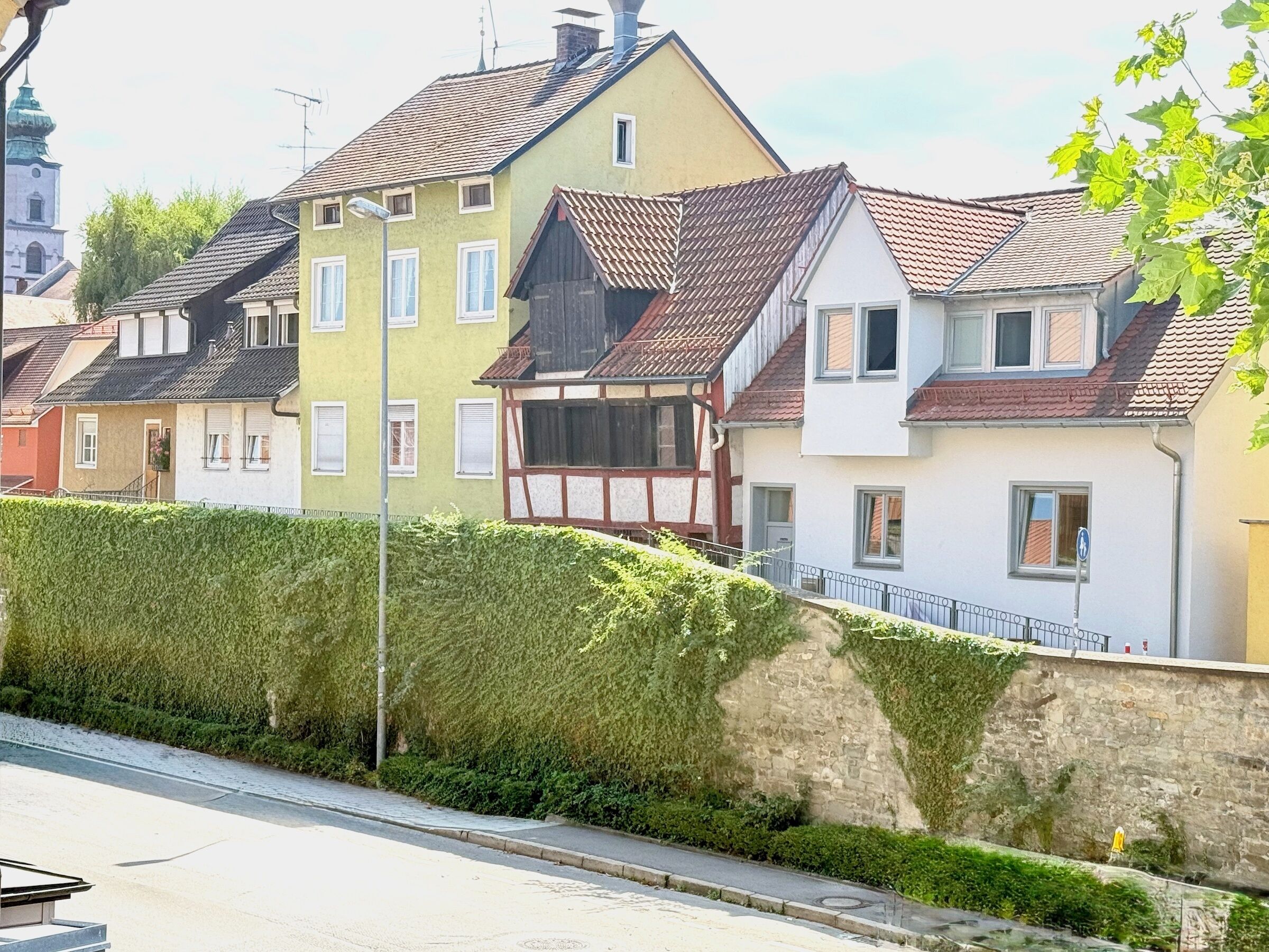 A row of traditional European-style houses with gabled roofs and a stone wall with greenery.
