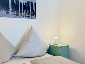 A bedroom with a bed, pillows, a nightstand with a lamp, and a wall-mounted picture. - "Inselwohnung" Vacation Rental - A Getaway by the Small Lake on the Island of Lindau (Lindau (Bodensee))