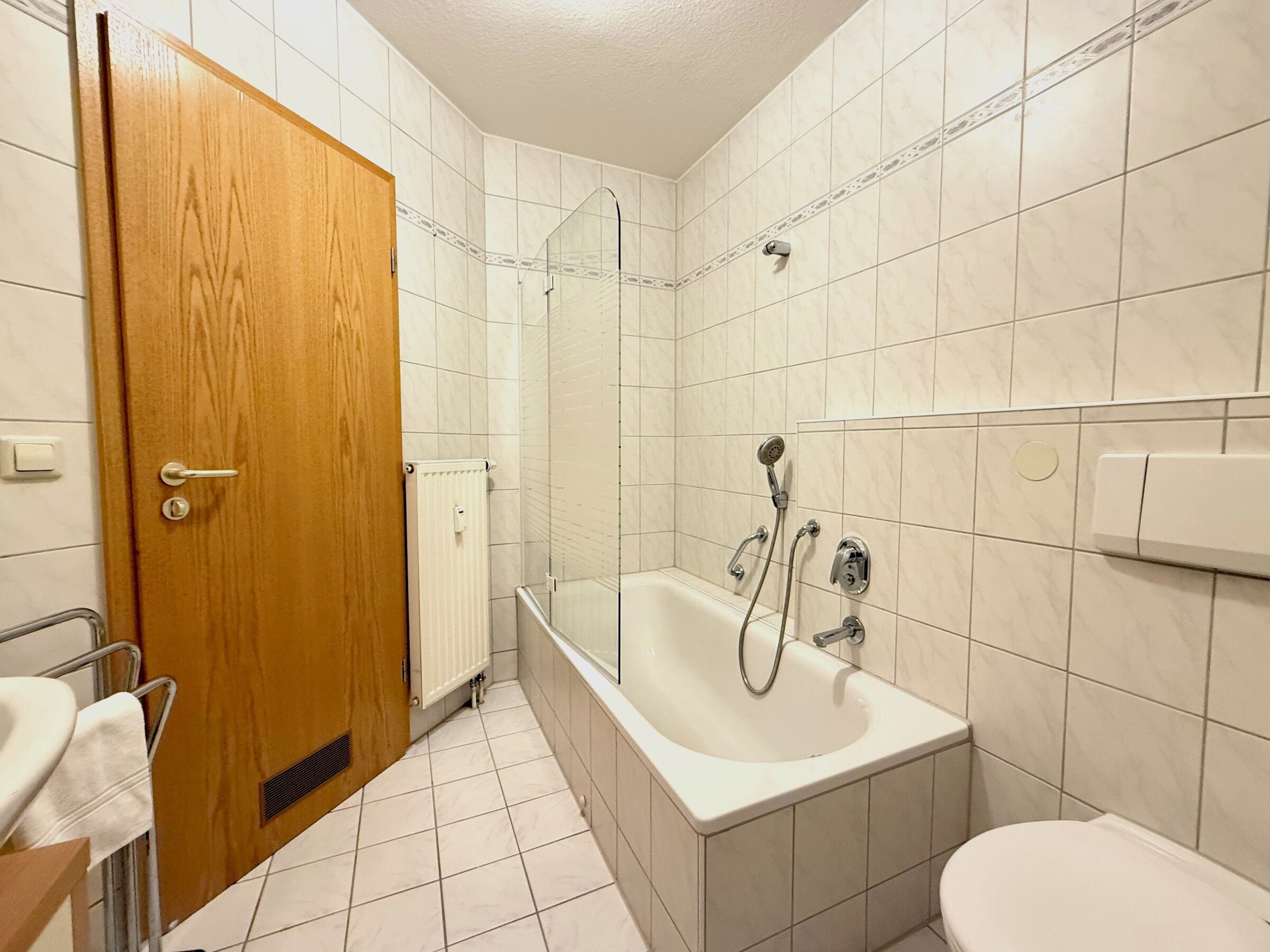 A bathroom with a wooden door, a bathtub, a shower, and a toilet.