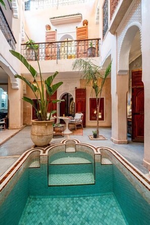 A pool area with a tiled floor, a seating area with chairs and a table, and a balcony with railings. - Riad Azura & Rooftop  (Marrakesh)