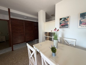 Un comedor con una mesa, sillas, un florero con flores y decoración en la pared.