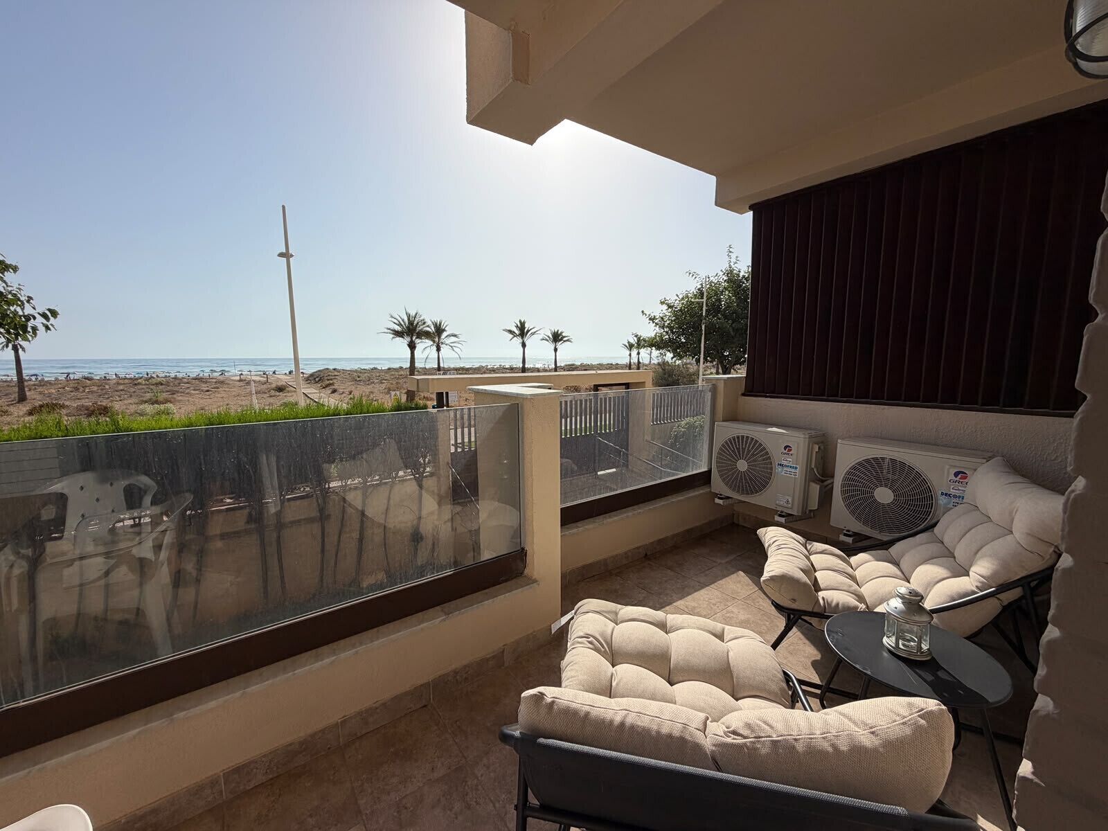 A balcony with a view of the beach, outdoor seating, and an air conditioning unit.