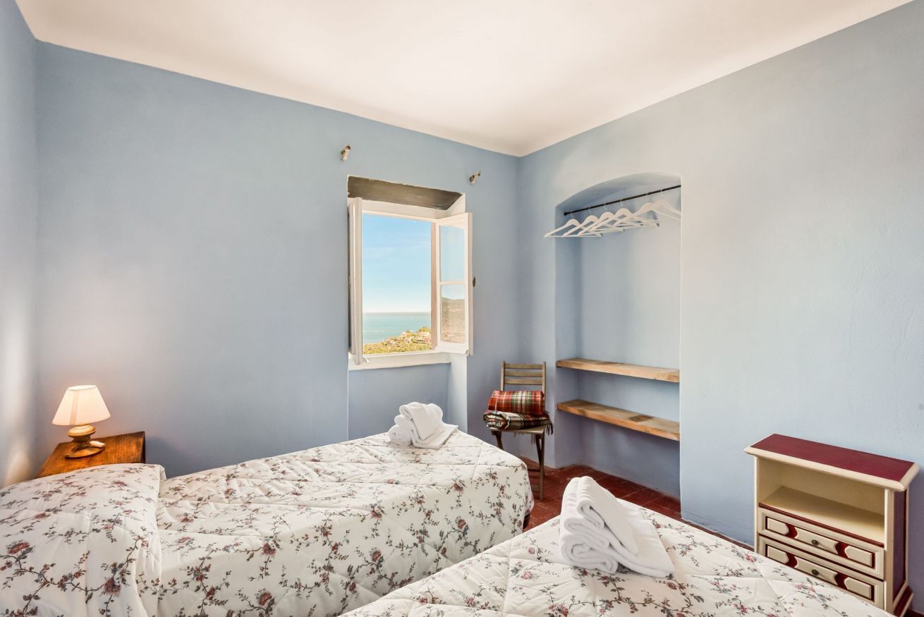 Une chambre avec deux lits, une fenêtre donnant sur un beau paysage, une chaise, une étagère et une table de chevet avec une lampe.