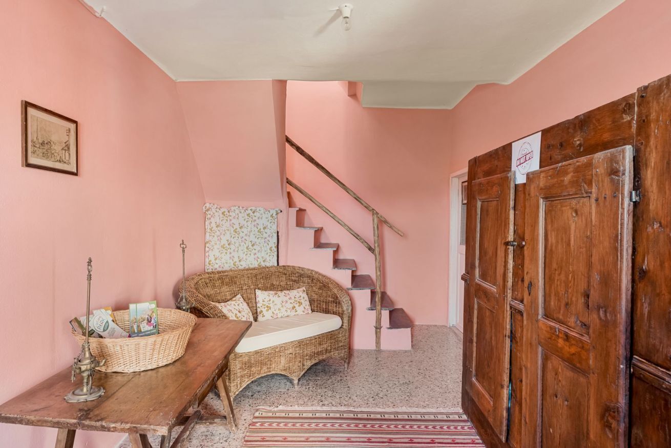 Une pièce avec un canapé en osier, une table en bois, un escalier et une porte en bois.