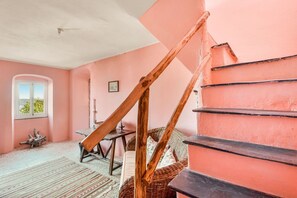 A room with a pink wall, a wooden staircase, a wicker sofa, and a small table. - [ilCeppo] 5Terre-Seaview-Parking (La Spezia)