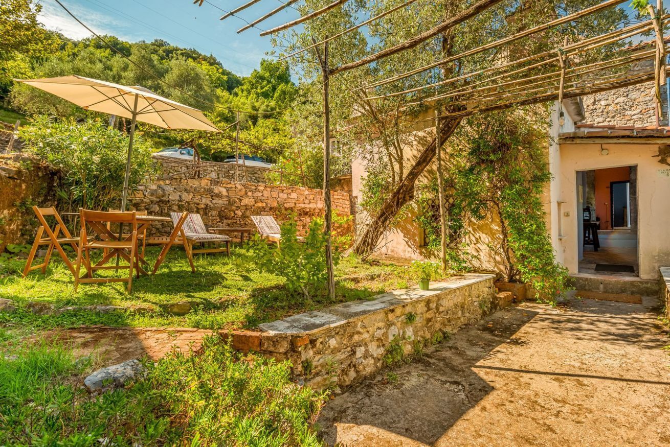 Un espace extérieur aménagé dans un style rustique, avec des murs en pierre, une pergola et une table entourée de chaises.