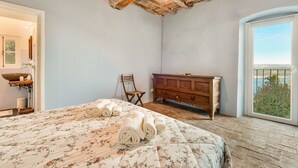 Ein Schlafzimmer mit einem Bett, einem Holzkapfen, einem Sessel, einem Waschbecken und Blick ins Freie.