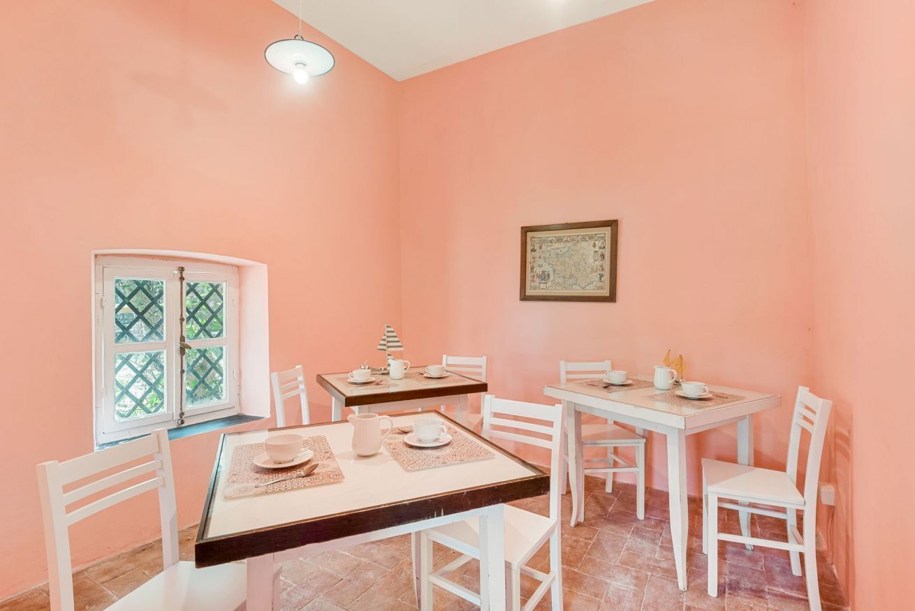 A dining area with two tables, white chairs, a window with a lattice design, and a framed map on the wall.