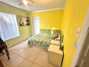A bedroom with a bed, a nightstand, a window with blinds, a door, and a ceiling fan. - Cute House in East Englewood (Port Charlotte Thorman Rd)