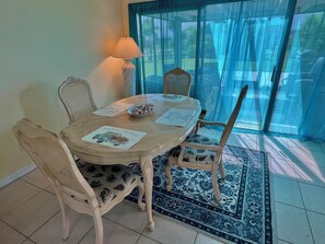 A dining area with a round table, four chairs, a lamp, and a view through a glass door. - Cute House in East Englewood (Port Charlotte Thorman Rd)