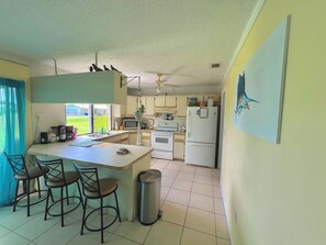 A kitchen with a central island, chairs, a trash bin, and a refrigerator. - Cute House in East Englewood (Port Charlotte Thorman Rd)
