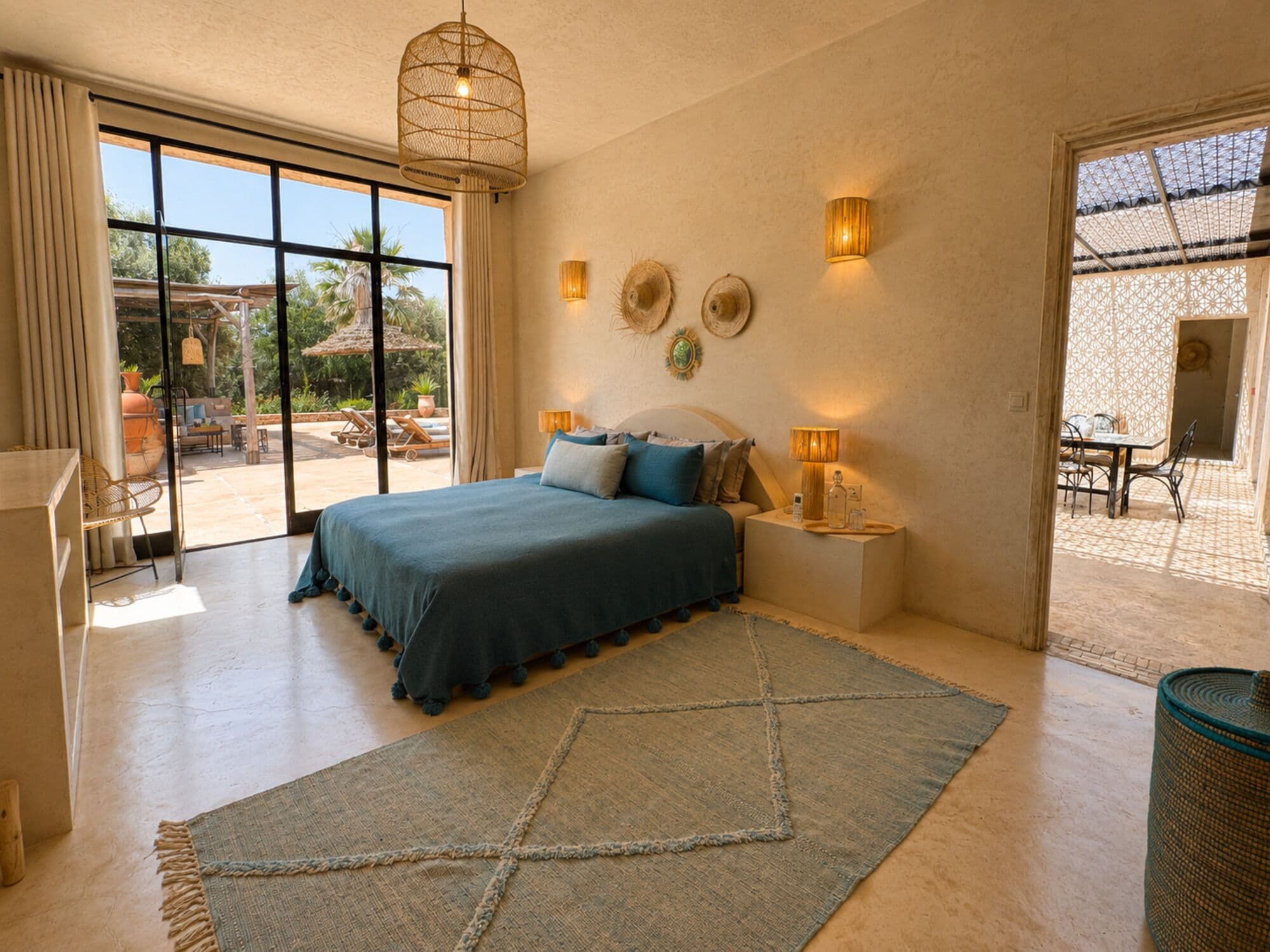 A bedroom with a large bed, a nightstand, a wall-mounted lamp, and a view of an outdoor patio.