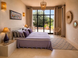 A bedroom with a large bed, bedside lamps, a painting, and a view of the outdoors.