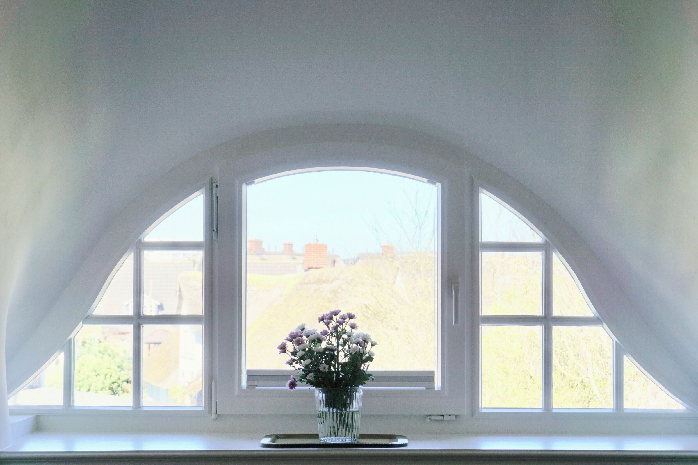 Une pièce dotée d’une grande fenêtre en arc de cercle et d’un vase rempli de fleurs posé sur un rebord de fenêtre.