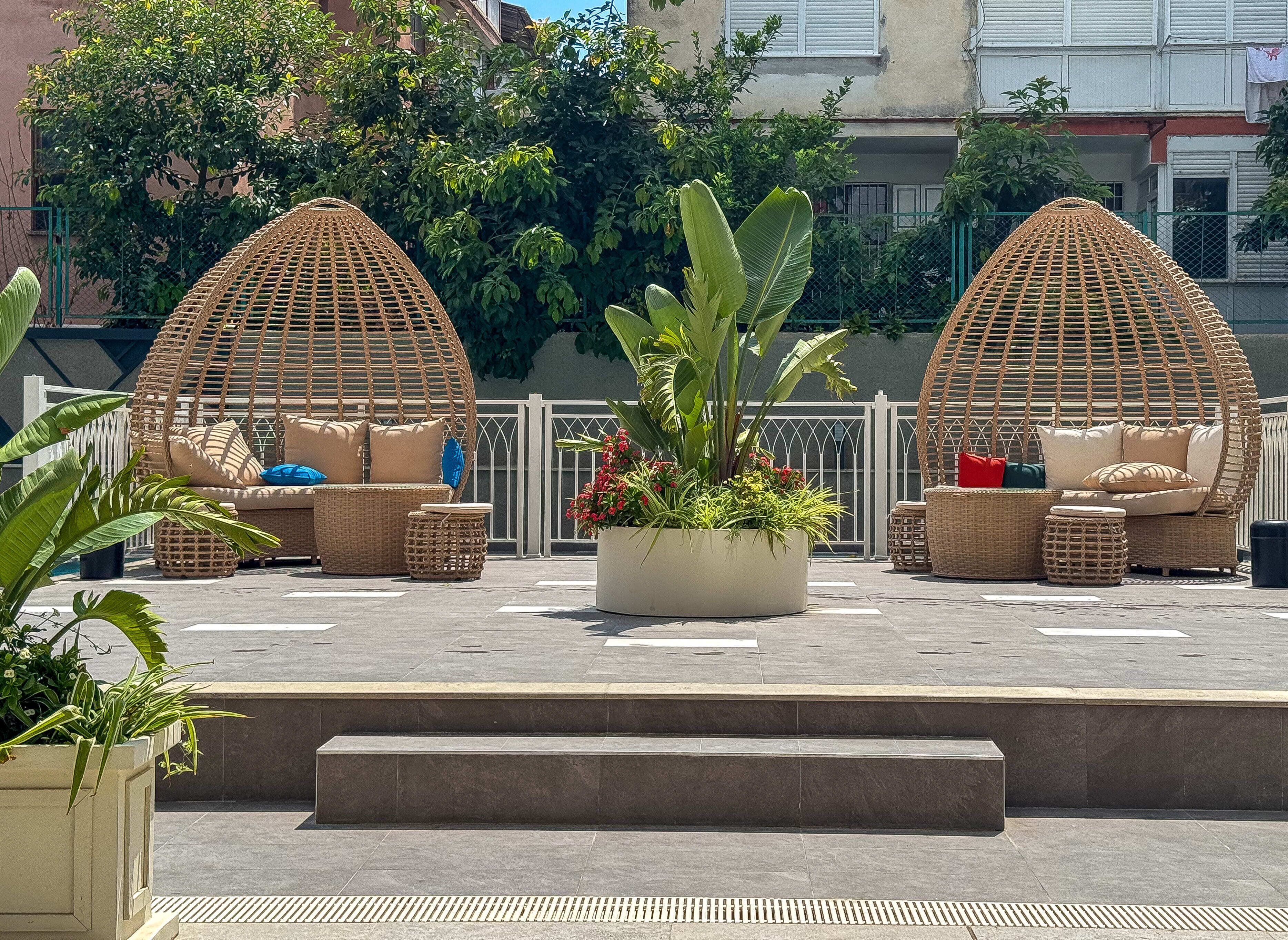 Une terrasse sur le toit comprenant deux coins salon avec des meubles en osier, un jardinier central planté, et une vue sur les bâtiments environnants.