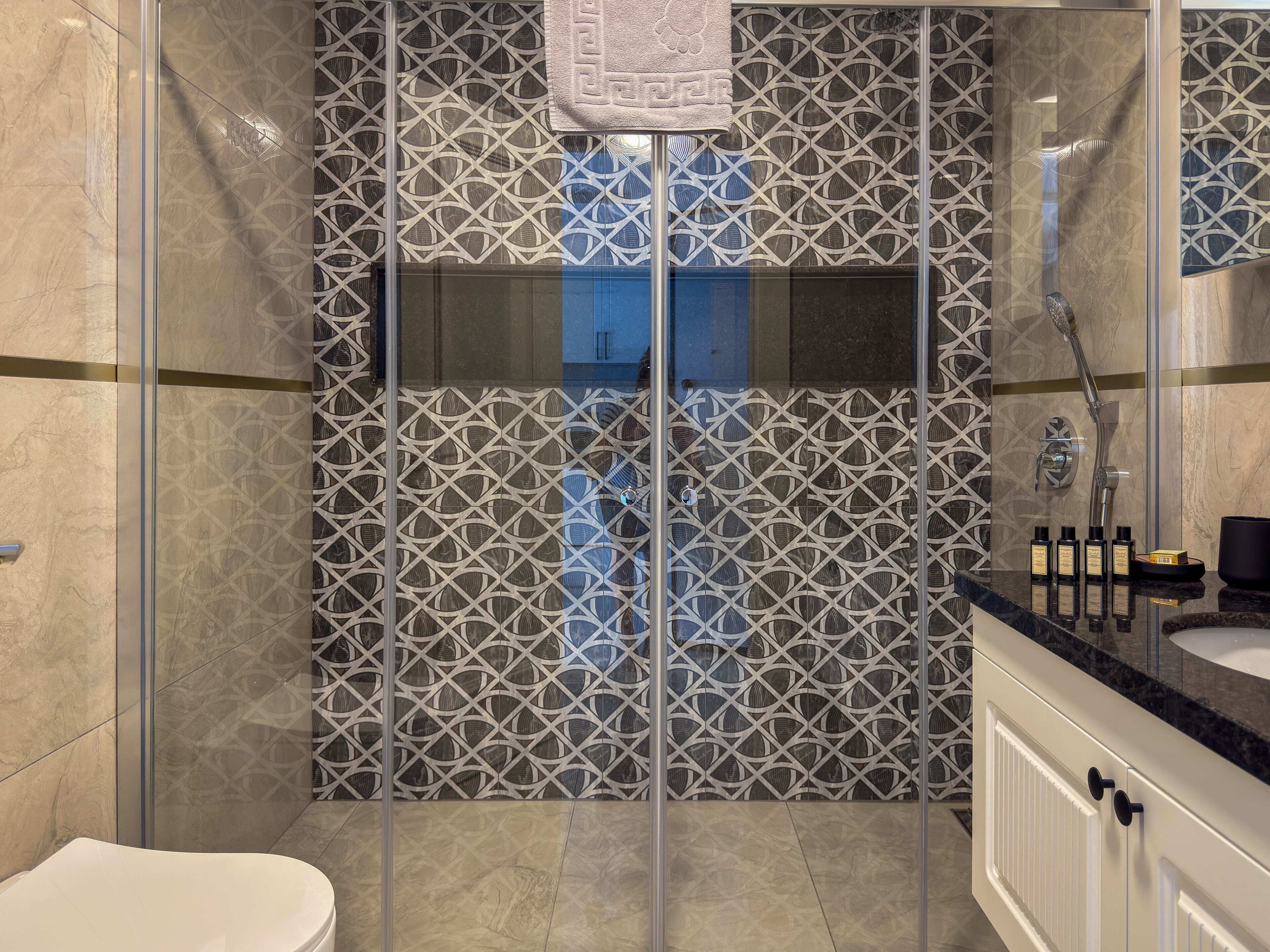 A modern bathroom with a glass shower enclosure, patterned tiles, and a vanity with toiletries.