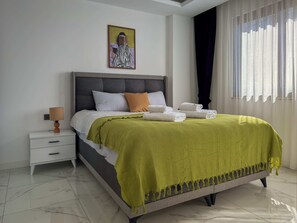A neatly made bed with a green blanket, a bedside lamp, and a painting on the wall. - Qoople Elize C9 - Cozy 1-bedroom apartment in Alanya (Alanya)