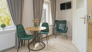 A room with a round table, two green chairs, a potted plant, and a window with curtains.