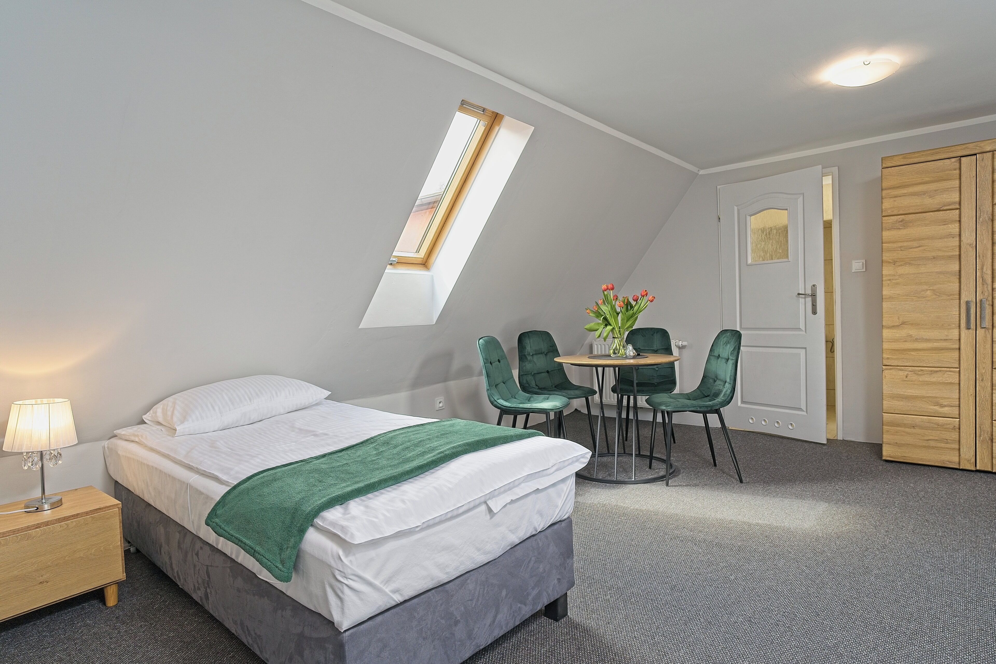 A bedroom with a bed, a nightstand, a table with chairs, a window, and a wardrobe.