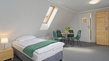 Un dormitorio con cama, mesita de noche, una mesa con sillas, una ventana y un armario.