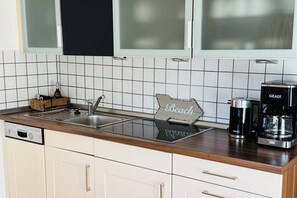 Ett kök med vita skåp, en träbänkskiva, ett handfat, en kaffebryggare och en dekorativ skylt.