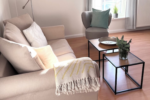 En stue med en beige sofa, et lille sofabord og en potteplante.