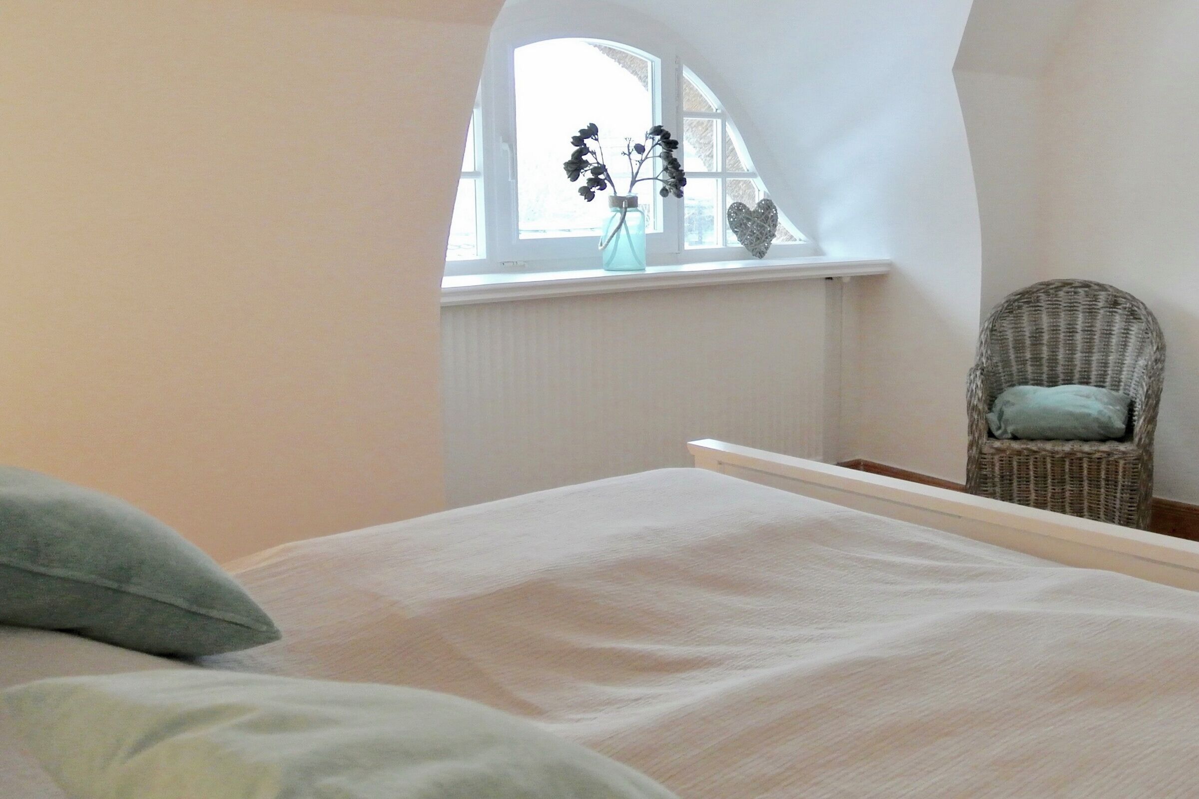 A bedroom with a bed, a chair, a window with plants, and a white wall.