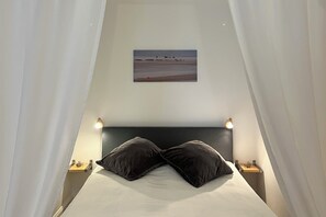 A bedroom with a bed, two bedside tables, a nightstand, a wall-mounted picture, and a curtain. - Vrbo Property (Sylt)