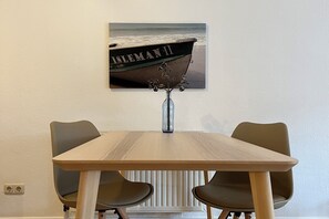 A dining table with two chairs, a vase with flowers, and a framed picture of a boat on the wall. - Vrbo Property (Sylt)