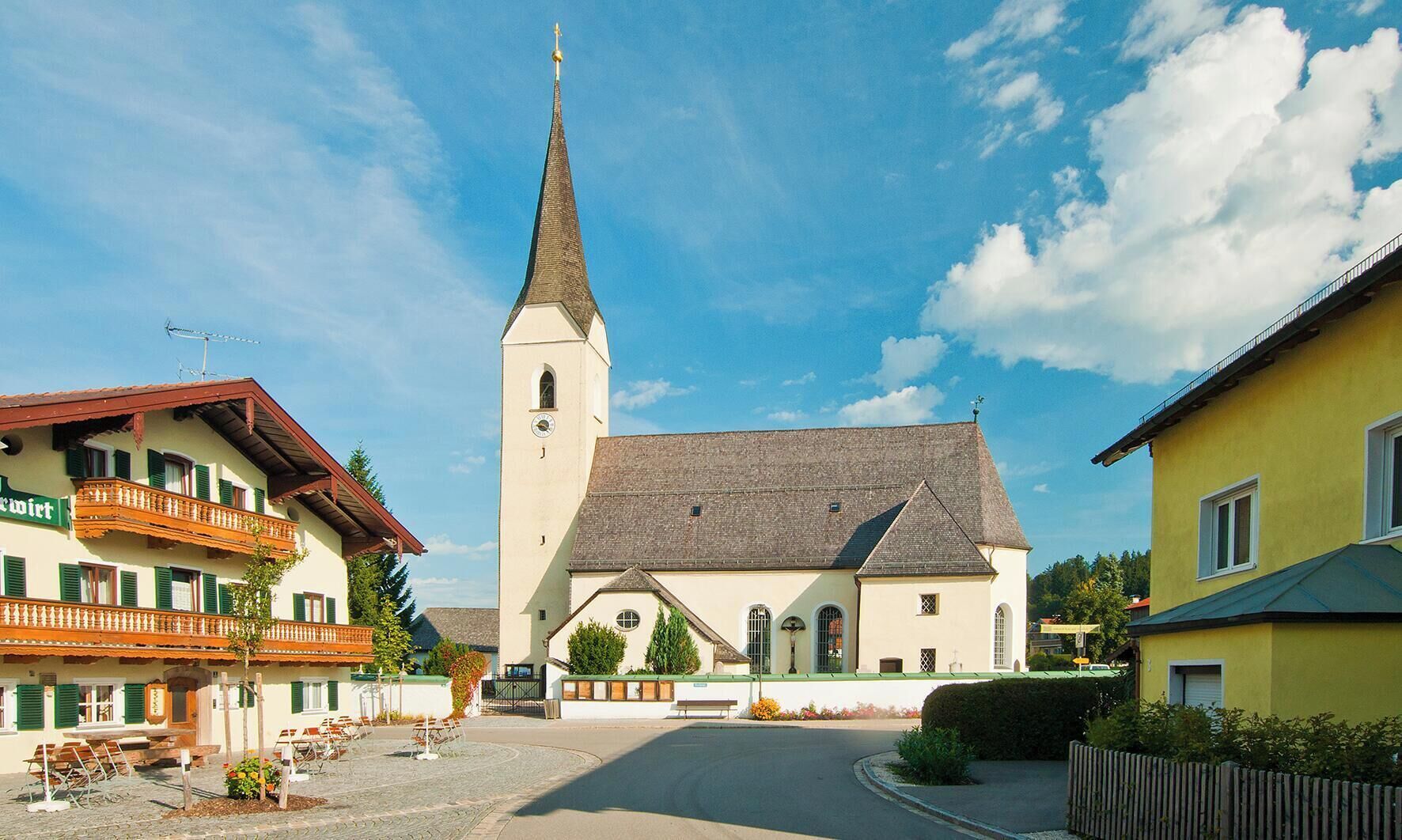 Eine Kirche mit einem hohen Kirchturm, ein Innenhof mit Bänken und ein Gebäude mit einem Balkon.
