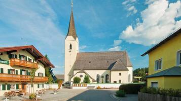 Eine Kirche mit einem hohen Kirchturm, ein Innenhof mit Bänken und ein Gebäude mit einem Balkon.