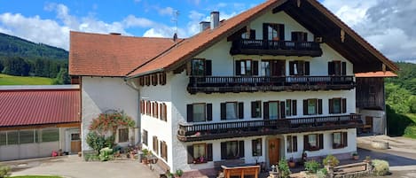 A two-story building with balconies, a red-tiled roof, and a garden area with potted plants.