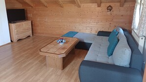 A cozy room with a wooden ceiling, a sofa with cushions, a wooden coffee table, and a television on a dresser.
