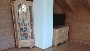 A room with wooden walls and a sloped ceiling, featuring a wooden cabinet with glass doors and a television on a wooden dresser.