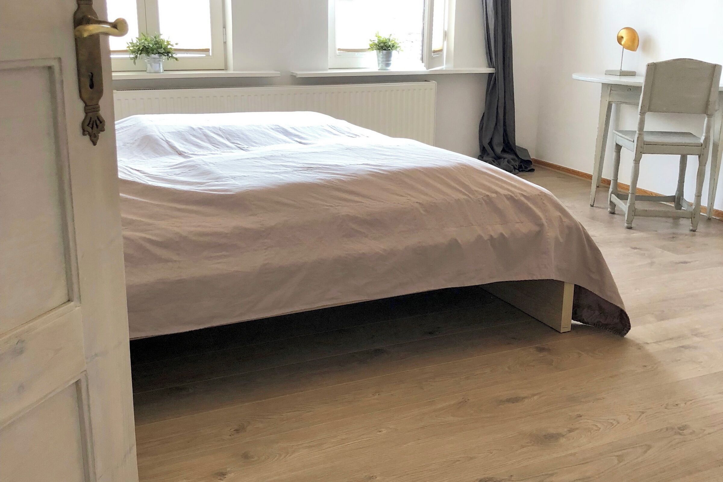 Une chambre à coucher avec un lit, un radiateur, une fenêtre avec des rideaux, un bureau et une chaise.