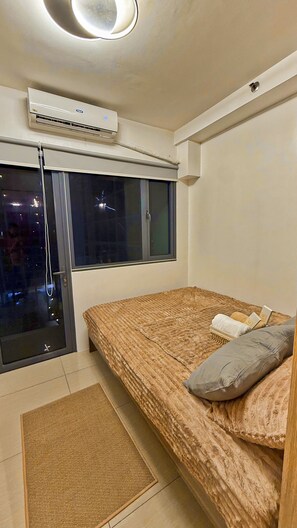 A bedroom with a bed, a window, an air conditioning unit, and a door. - Shore 2 Cozy Staycation, Pool View, Near MOA and NAIA Airport w/ Netflix (Pasay City)
