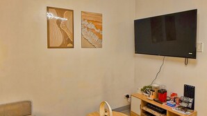 A modern living room with a flat-screen TV mounted on the wall, a round coffee table with a lamp, and a sofa. - Shore 2 Cozy Staycation, Pool View, Near MOA and NAIA Airport w/ Netflix (Pasay City)