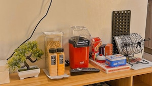 A wooden desk with a computer monitor, a red appliance, a BINGO set, a Rubik's Cube, and a wooden word game. - Shore 2 Cozy Staycation, Pool View, Near MOA and NAIA Airport w/ Netflix (Pasay City)