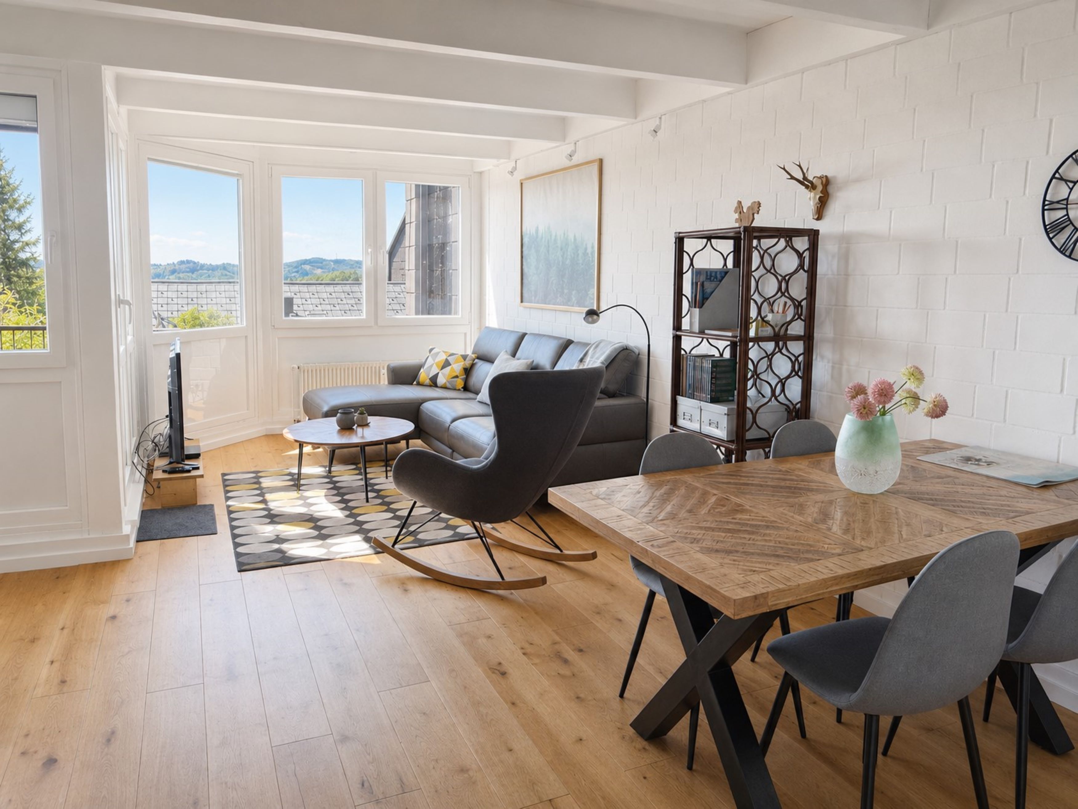 Ein modernes Wohnzimmer mit einer Couch, einem Esstisch und Blick durch große Fenster.