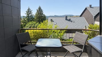 Ein Balkon mit zwei Stühlen und einem Tisch, der einen Wohnbereich mit Häusern und Bäumen blickt.