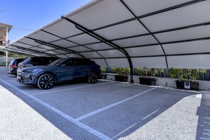 En parkeringskælder med et overdækket område, en blå bil parkeret indeni og plantekasser langs væggen.
