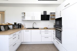 Uma cozinha moderna com armários brancos, exaustor preto, forno embutido e máquina de café.