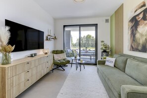 En moderne stue med et fladskærms-TV, en grøn sofa, et sofabord og udsigt gennem en glasdør.
