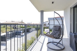 Ein Balkon mit einer Hängematte, Blick auf einen Parkplatz und ein Gebäude im Hintergrund.
